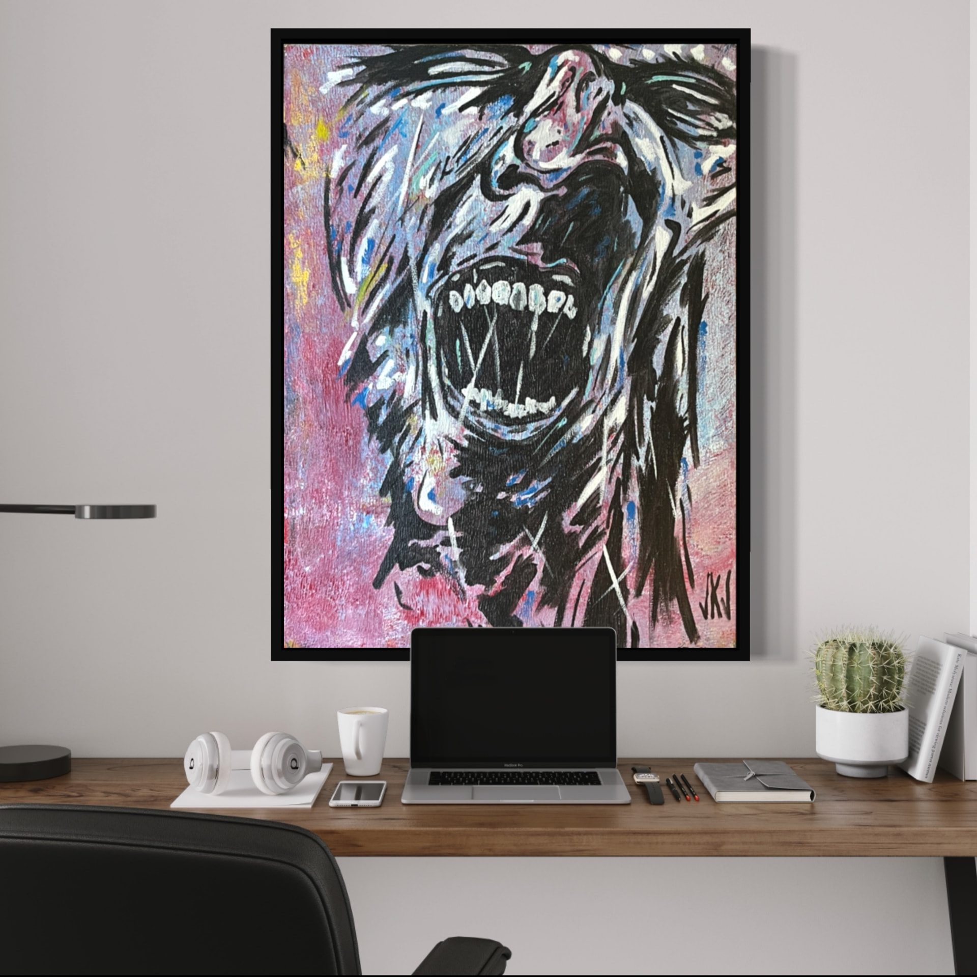 Painting of a screaming face hung above a home office desk with a laptop and headphones